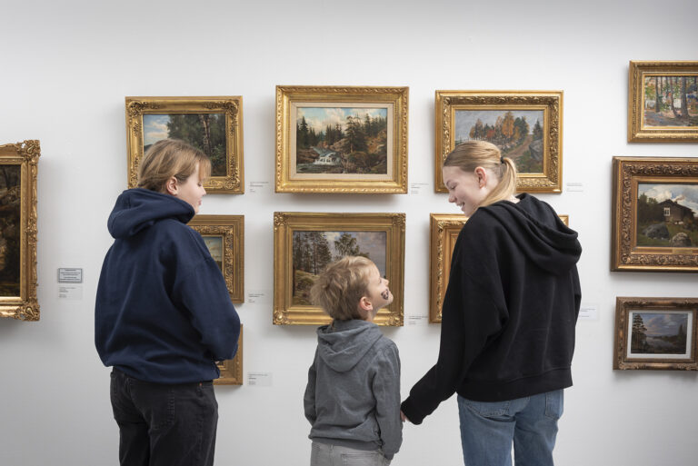 Kolme lasta keskustelevat taideteosten äärellä.