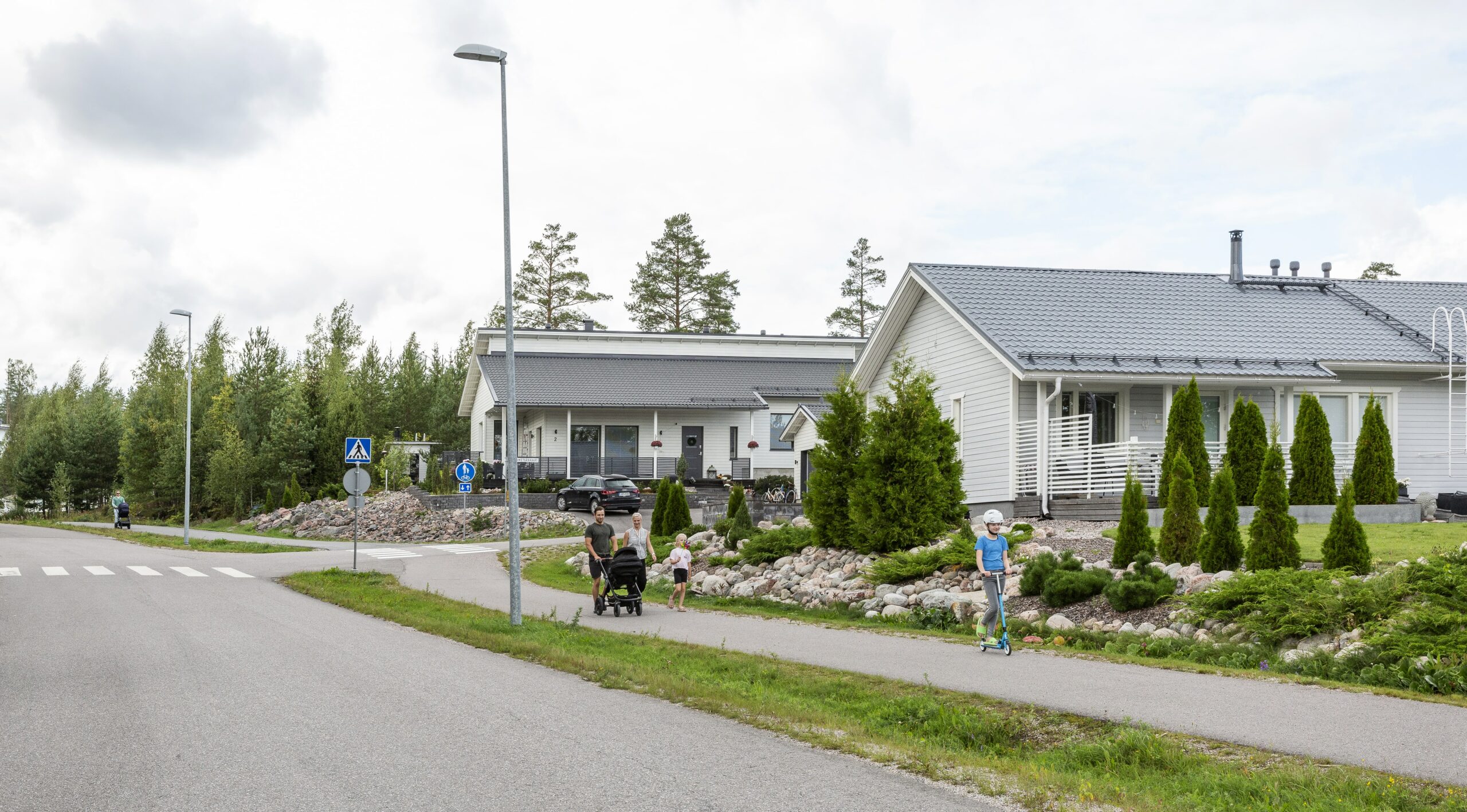 Perhe kävelemässä jalkakäytävällä asuinalueella.