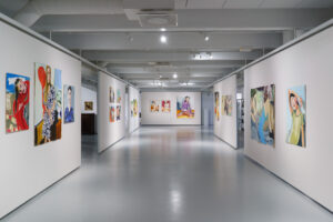Kuva näyttelytilasta, jossa teoksia on ripustettu seinäkkeille.